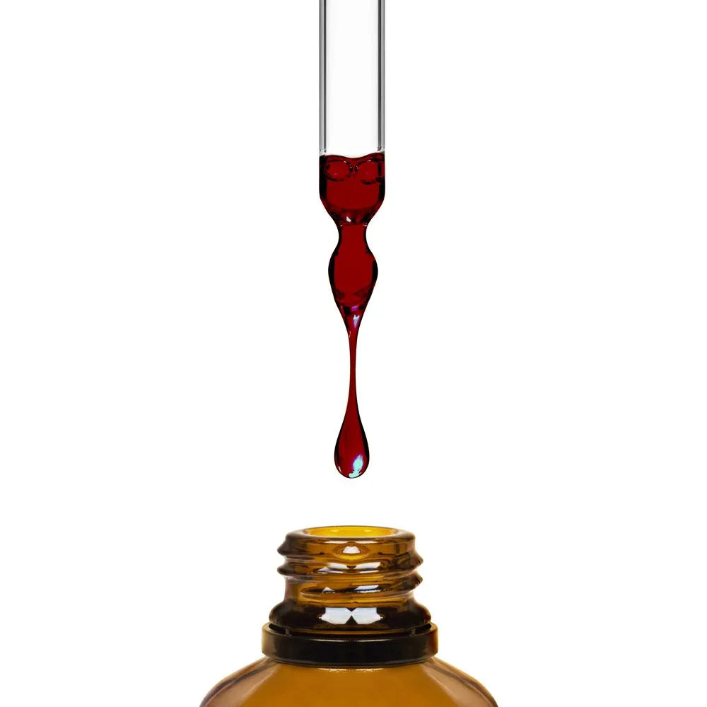 A glass dropper dispensing dark purple elderberry syrup from the Nuusero Elderberry Defense bottle.